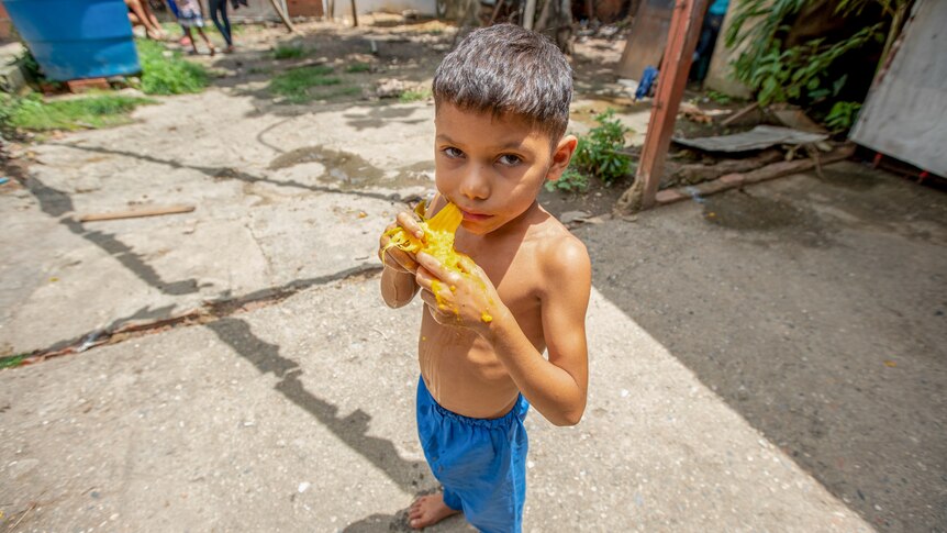 A little shirtless boy eating a mango