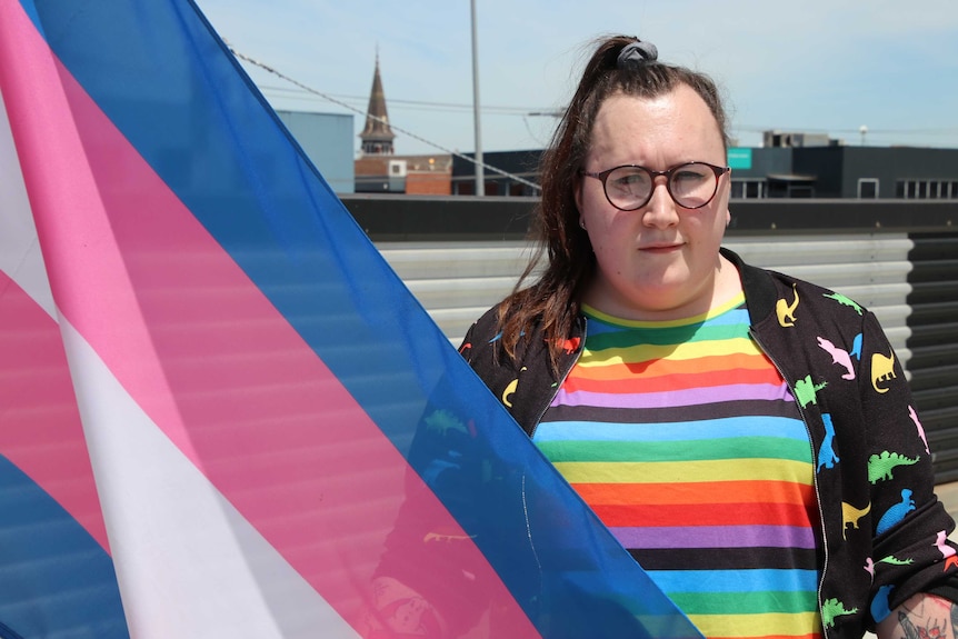 A woman smiles at the camera holding the transgender pride flag