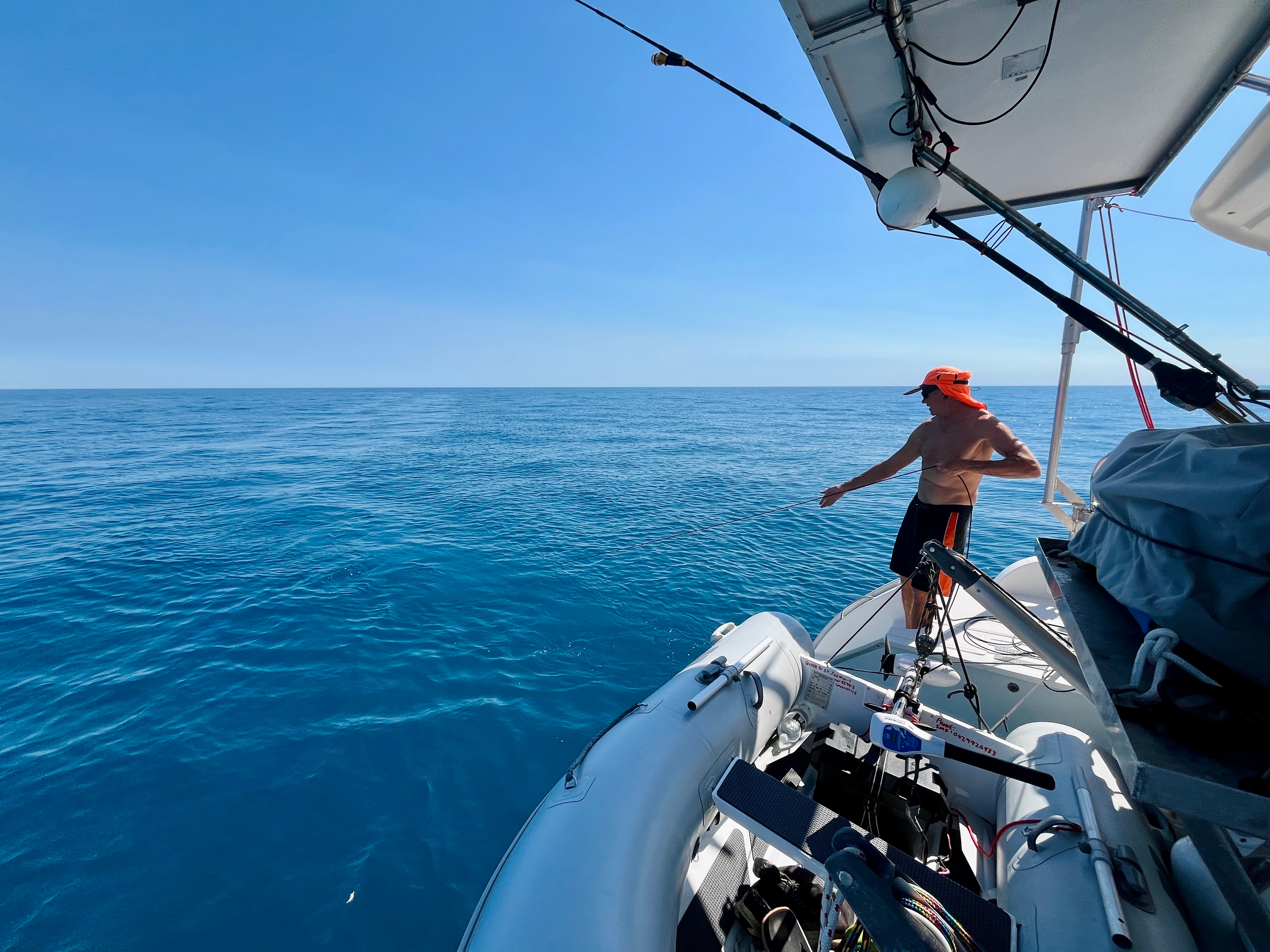 A man stands on a boat in the blue ocean, holding a cord.