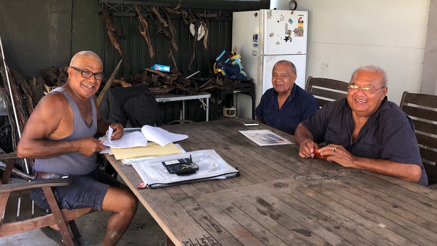 Three men from the Togo family seated around a table in a shed in the backyard