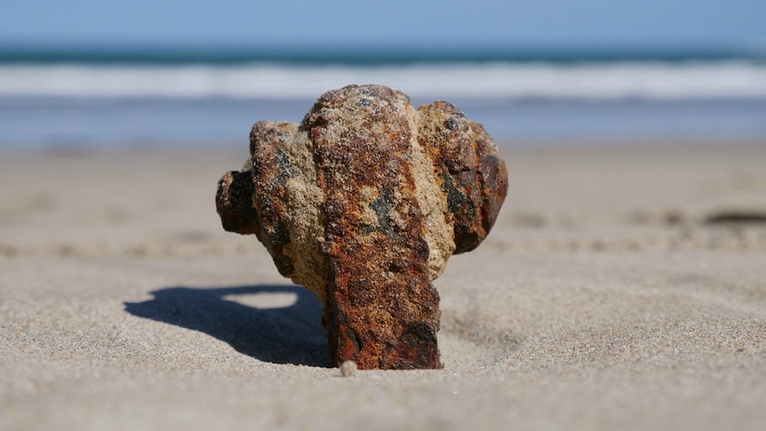 A rusted piece of metal rigging protrudes from the beach sand.