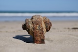 A rusted piece of metal rigging protrudes from the beach sand.