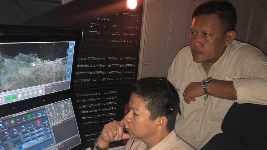 Two men look at a flight simulation on a screen.