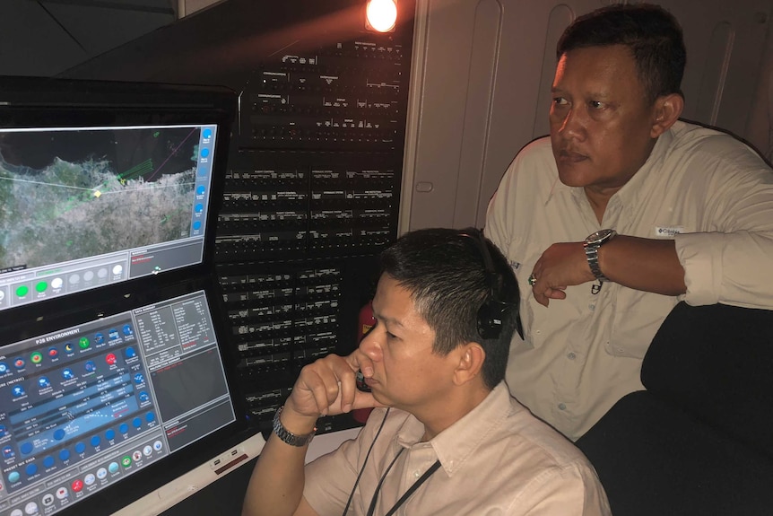 Two men look at a flight simulation on a screen.