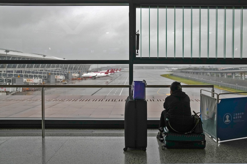 Pasażerka siedzi na swoim bagażu, obserwując zaparkowane na płycie samoloty pasażerskie