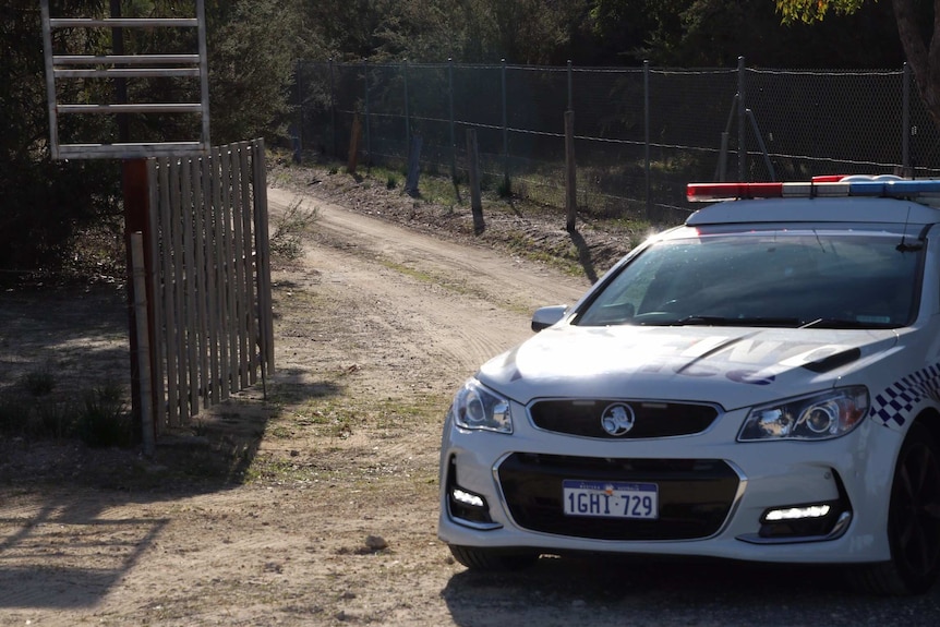 A police car parked next to a gate at the end of a dirt track.