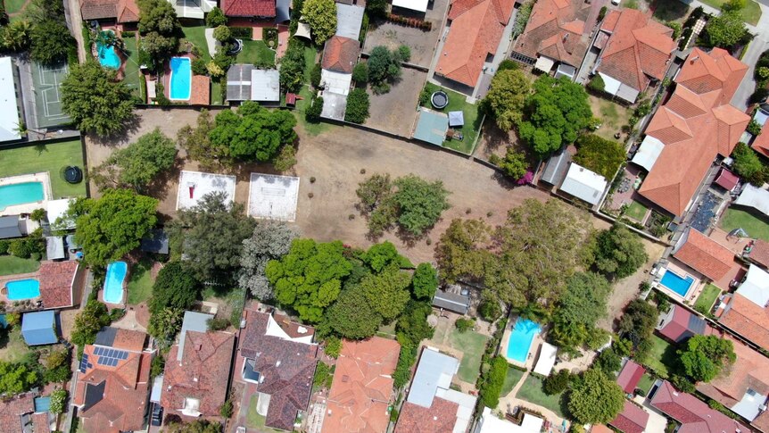 An aerial shot of a dry desolate park surrounded by dozens of large houses with swimming pools