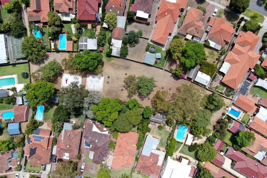 An aerial view of a desolate, dry park surrounded by dozens of large houses with swimming pools