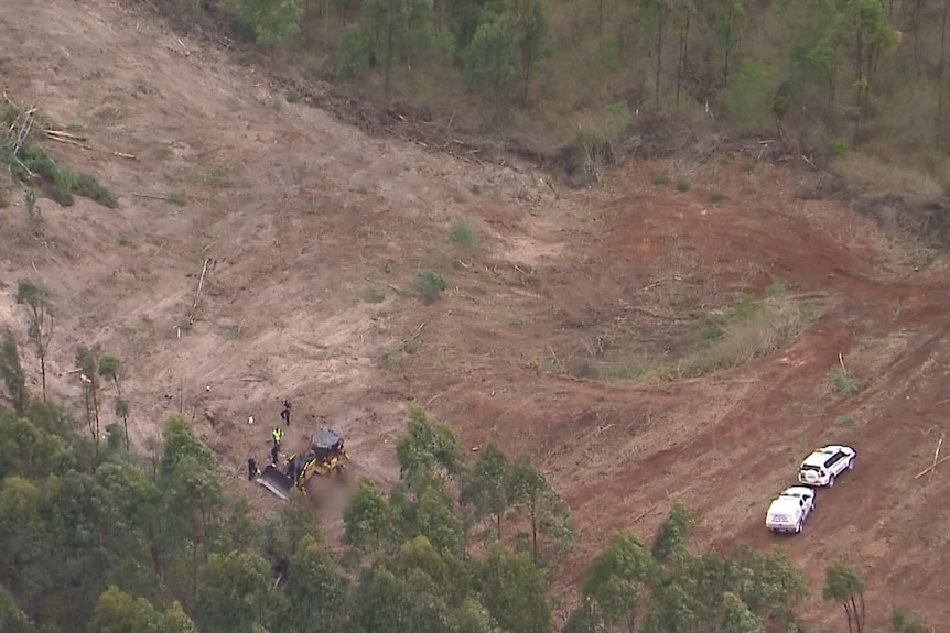 A large field with a bulldozer and police cars on it