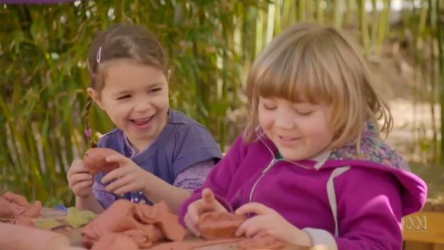 Two young girls play with clay at outdoor table