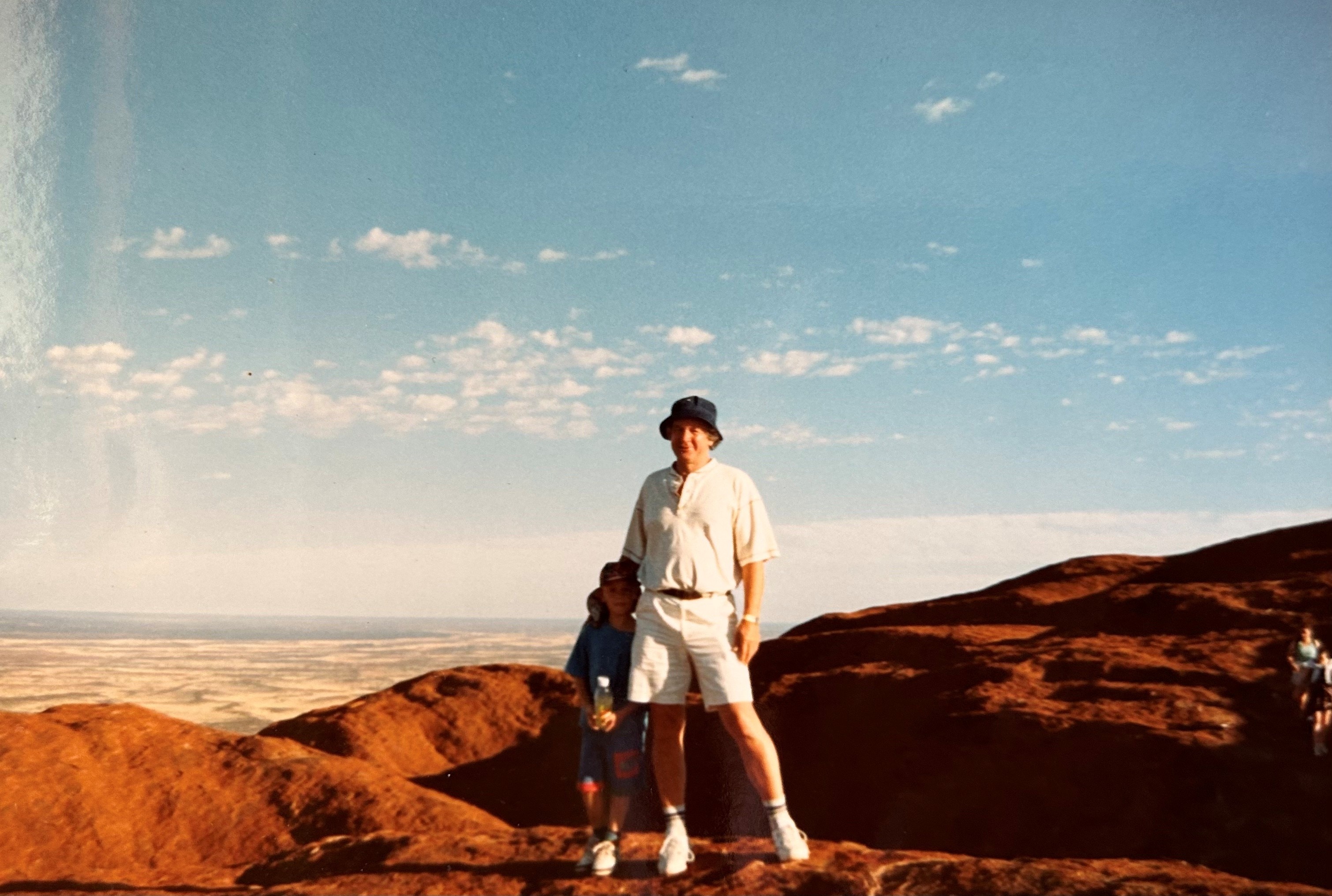 Um homem e uma criança pequena em pé em uma montanha com um vale ao fundo.