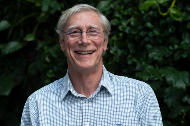 Mann mit grauem Haar und Brille lächelt und trägt ein Businesshemd