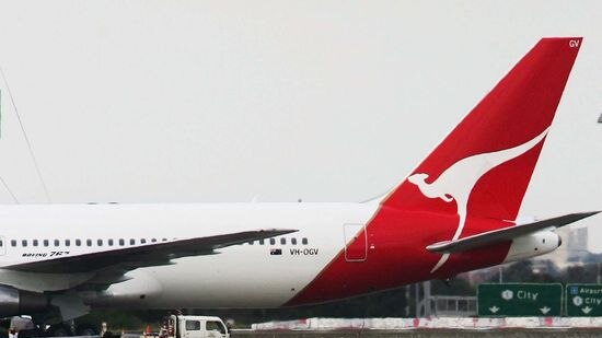 A Qantas jet taxis above a motorway at Sydney Airport.