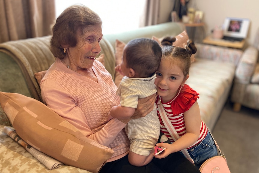 A woman smiles with a baby and a young girl on her lap.