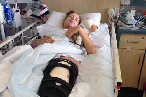 A woman lies on a hospital bed holding a white teddy.