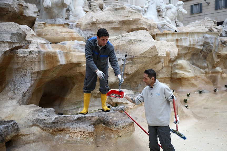 Two utility workers scoop up coins from Trevi Fountain while it is drained