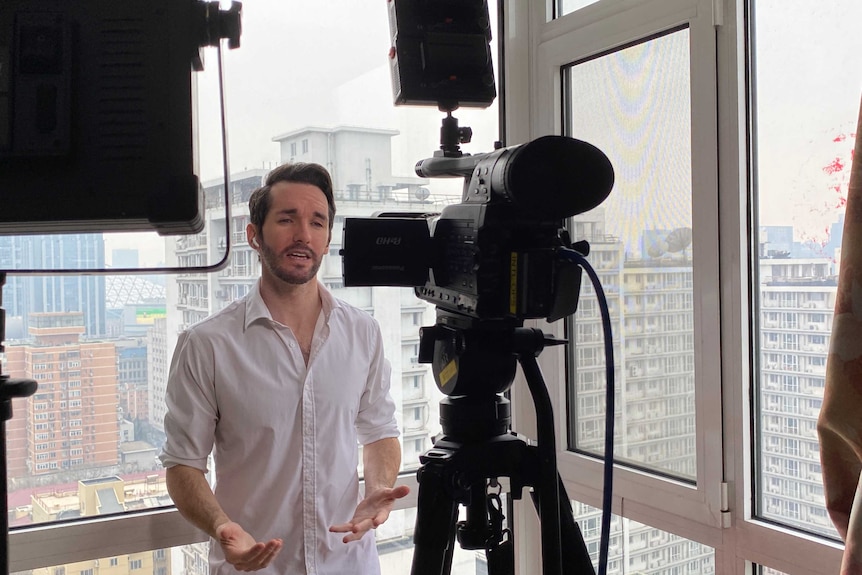 Bill Birtles standing in front of an apartment window speaking to a camera