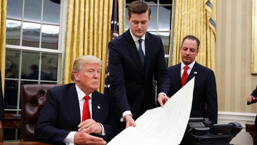 White House Staff Secretary Rob Porter hands President Donald Trump a confirmation order.