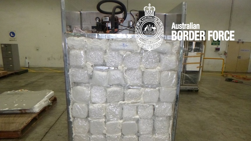 The rear of a fridge, with the back panel removed to reveal vacuum-packed bags of a white crystal substance.