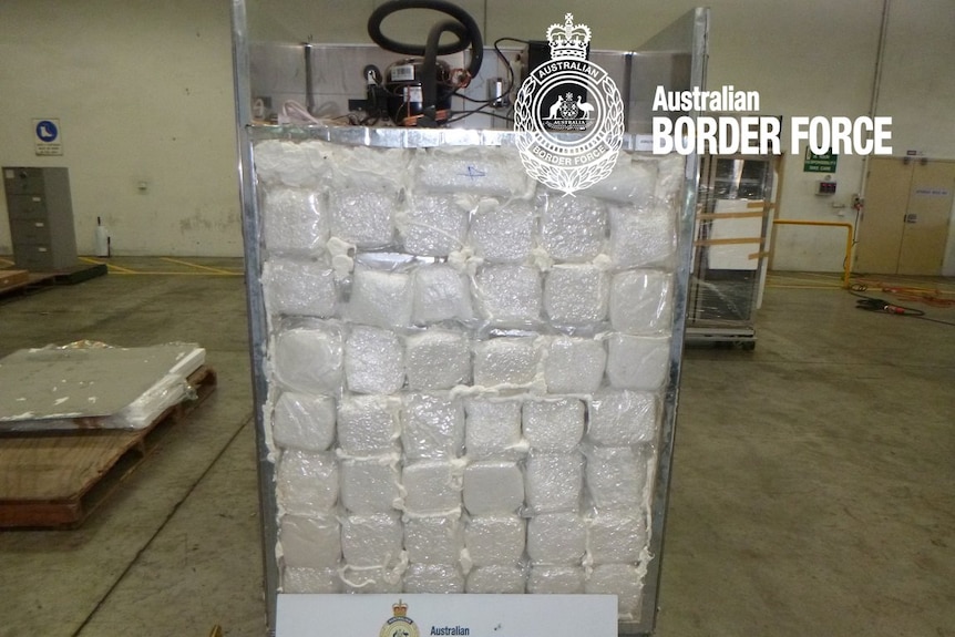 The rear of a fridge, with the back panel removed to reveal vacuum-packed bags of a white crystal substance.