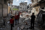 Palestinian children in foreground of photo walk amid the rubble of a house that was hit by Israeli airstrikes in Gaza City