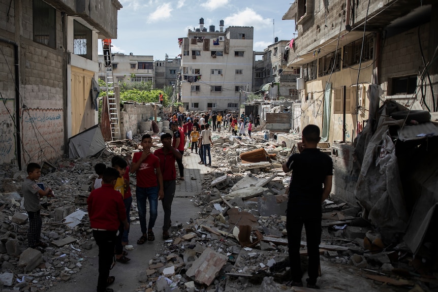Palestinian children in foreground of photo walk amid the rubble of a house that was hit by Israeli airstrikes in Gaza City