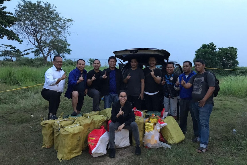 A large group of plain-clothes Indonesian police stand around a pile of bags of drugs.