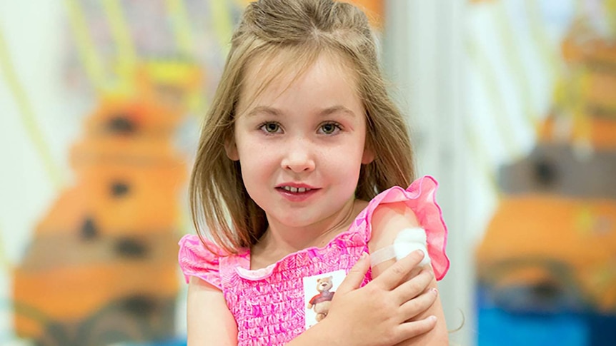 A young girl in pink dress holds her arm with a band-aid after receiving a flu shot.