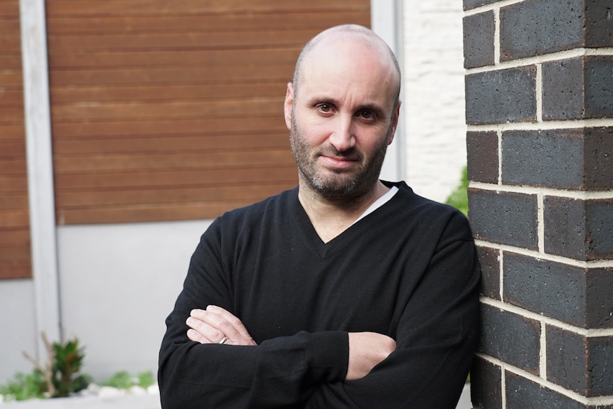 Adam Glezer leans against a brick wall with his arms crossed.