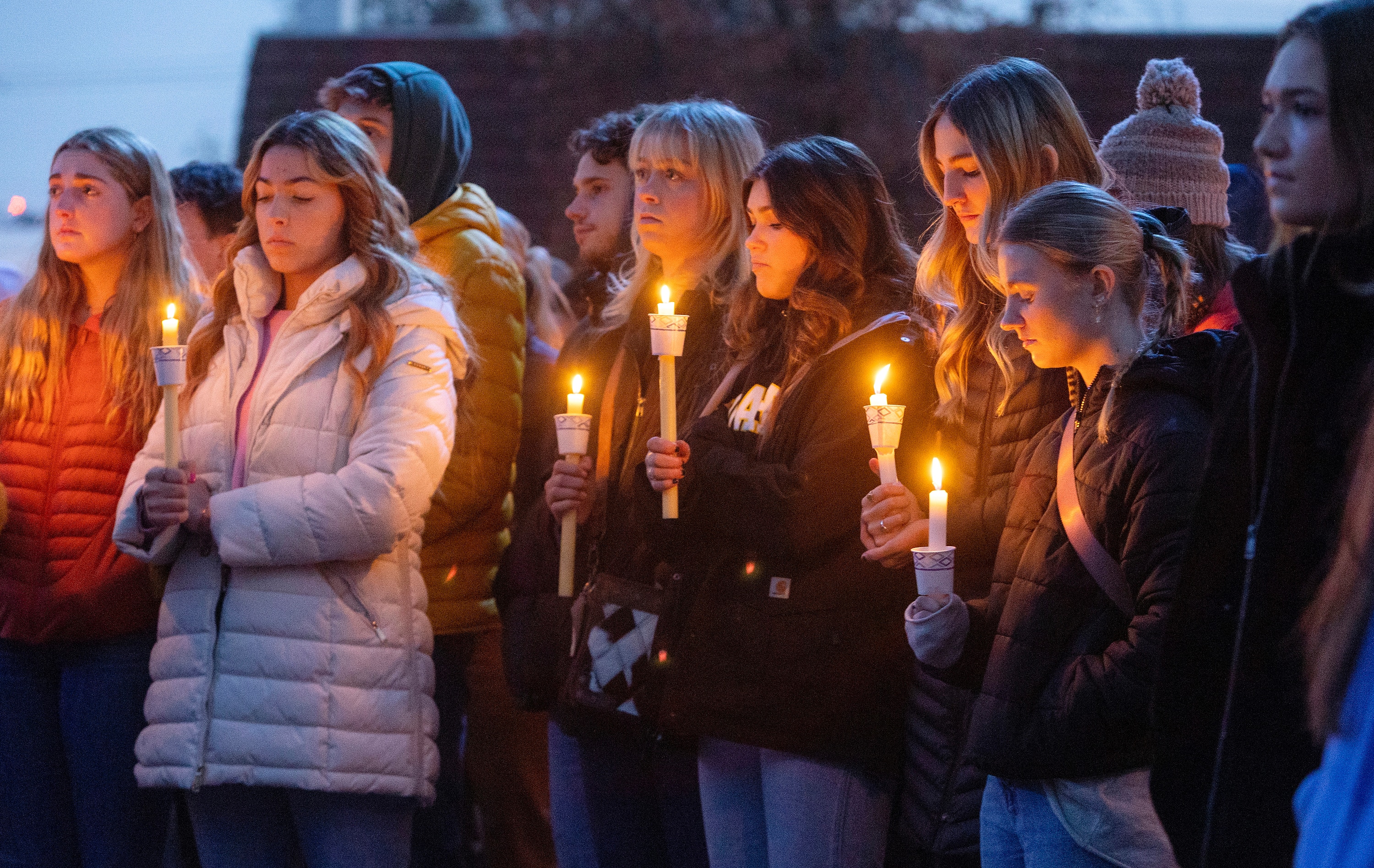 A group of female students in winter clothes stand together holding candles in vigil