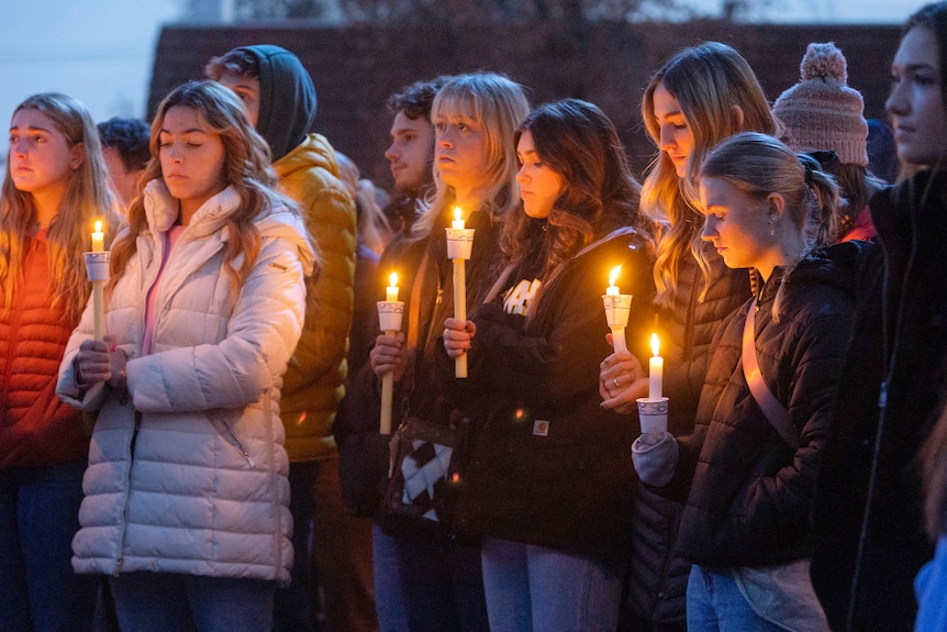 A group of female students in winter clothes stand together holding candles in vigil
