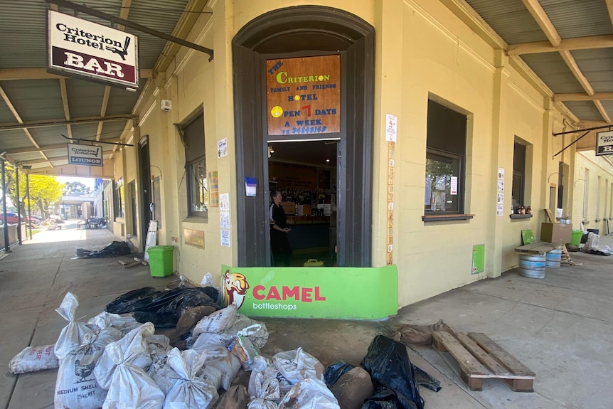 An old triangle building on a corner, with a bar sign, sand bags in front.