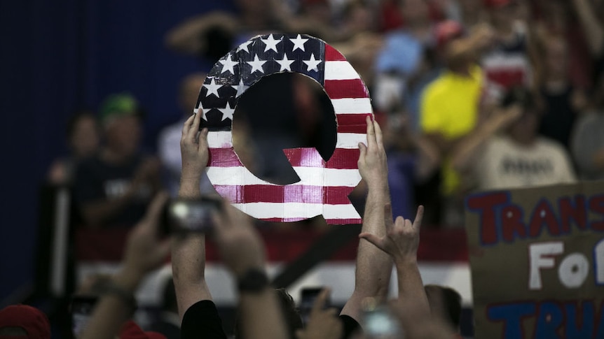 An attendee holds signs a sign of the letter "Q" before the start of a MAGA rally.