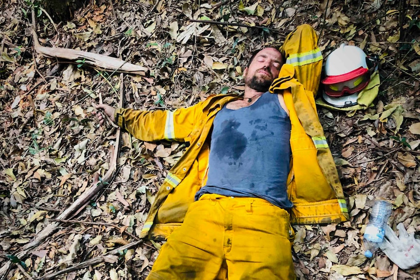 A man in yellow protective clothing asleep on the forest floor.