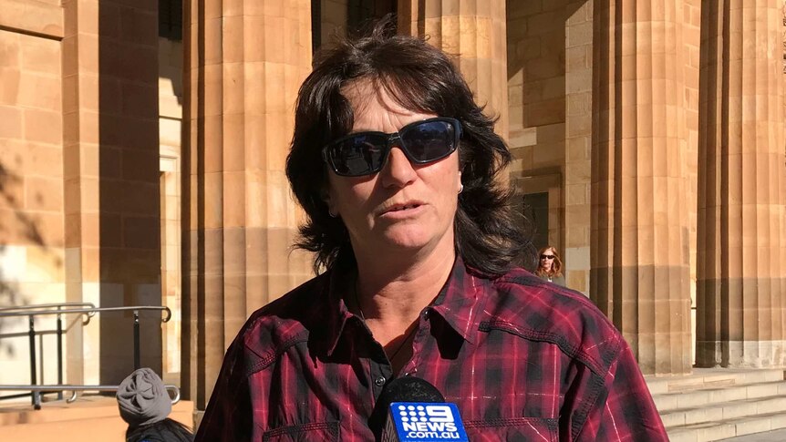 a woman in a red check shirt outside a court building.