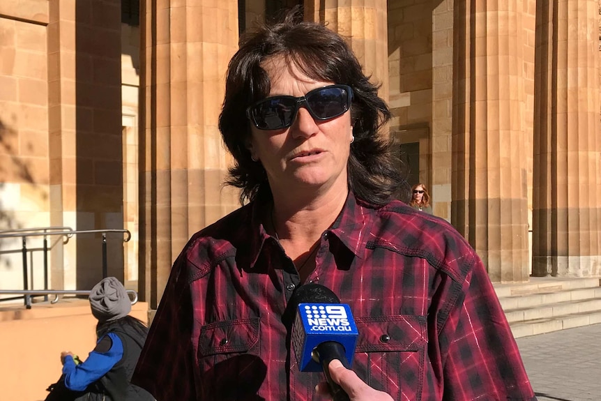 a woman in a red check shirt outside a court building.