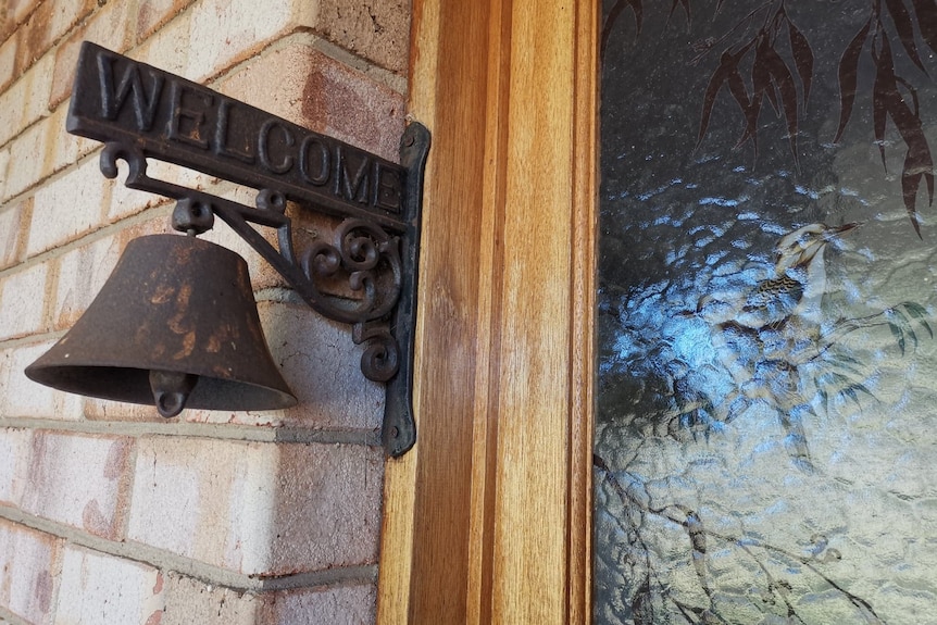 A cowbell hanging on the front door with welcome written above it. 
