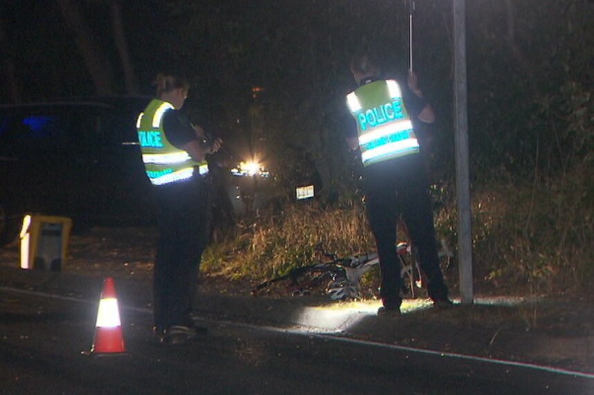 Two police officers shine a touch over the remains of a bike involved in a hit a run.