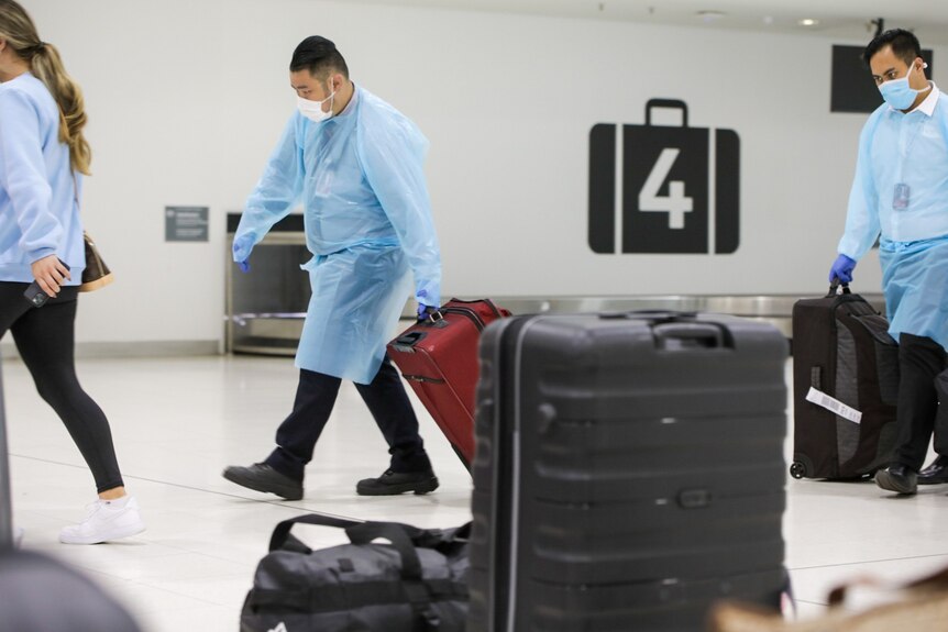 Two men in PPE wheel suitcases.