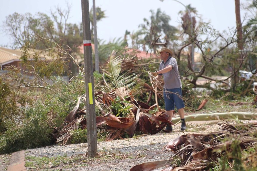 A man carries a tree branch to stack on a pile after Cyclone Damien. There are branches everywhere.