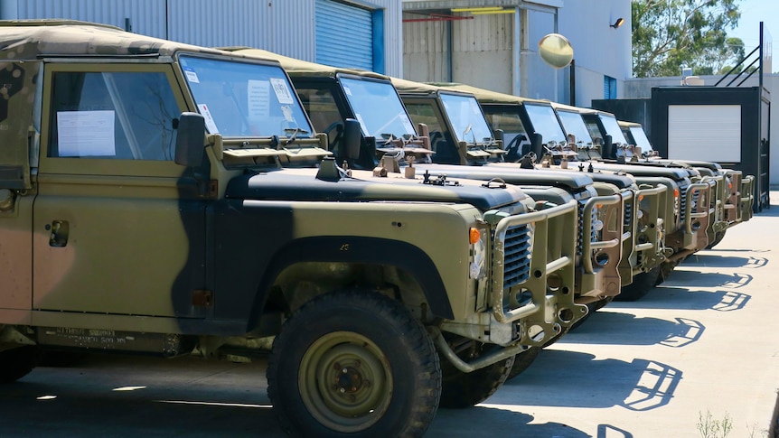 A line of land rover perenties parked at the Australian frontline machinery site, all cars are camouflaged 