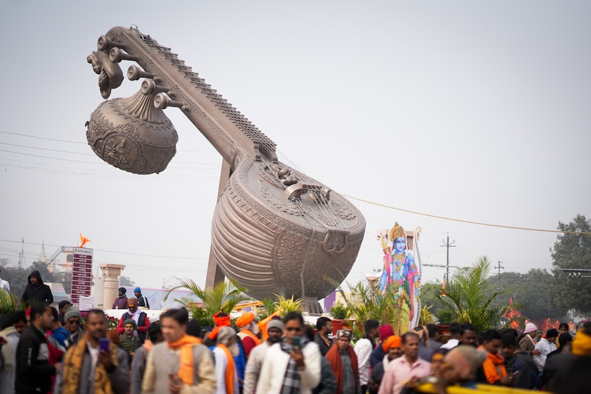 Crowds of people walk past a statue of a giant silver sitar