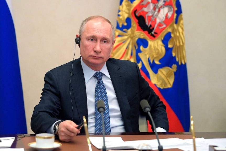 Russian President Vladimir Putin looks forward while listening through a headphone.