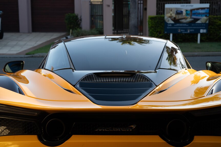 An orange sports car seen from behind with palm trees reflected in the windows.