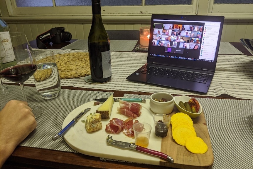 A cheese platter and wine in front of a laptop with zoom chat.