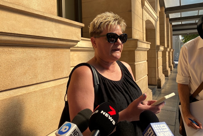 A woman with short blonde hair wearing a black dress outside a stone building