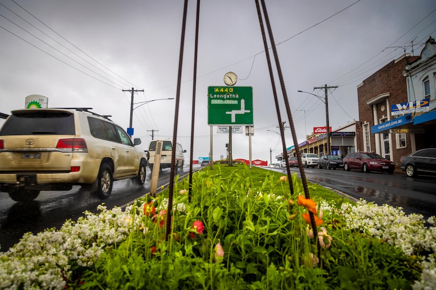 Korumburra shopping street, traffic island with flowers, dirty 4WD on left, road sign to Leongatha