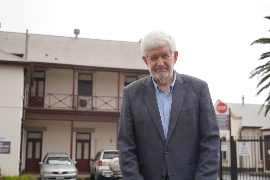 An elderly man standing infront of buildings wearing a tux 