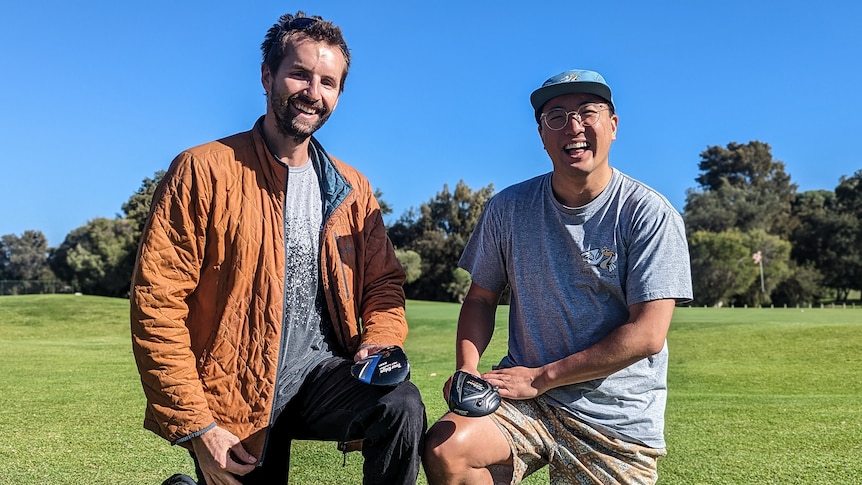 Dan Kohlman and Aaron Lee smiling and kneeling on a golf course and holding golf clubs 