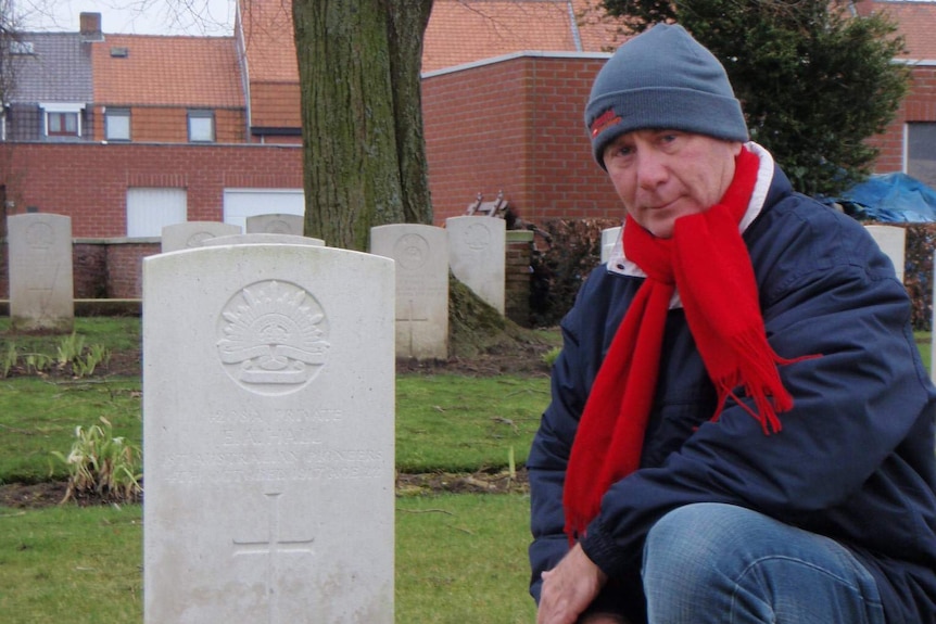 A man kneels next to a headstone in a cemetery.